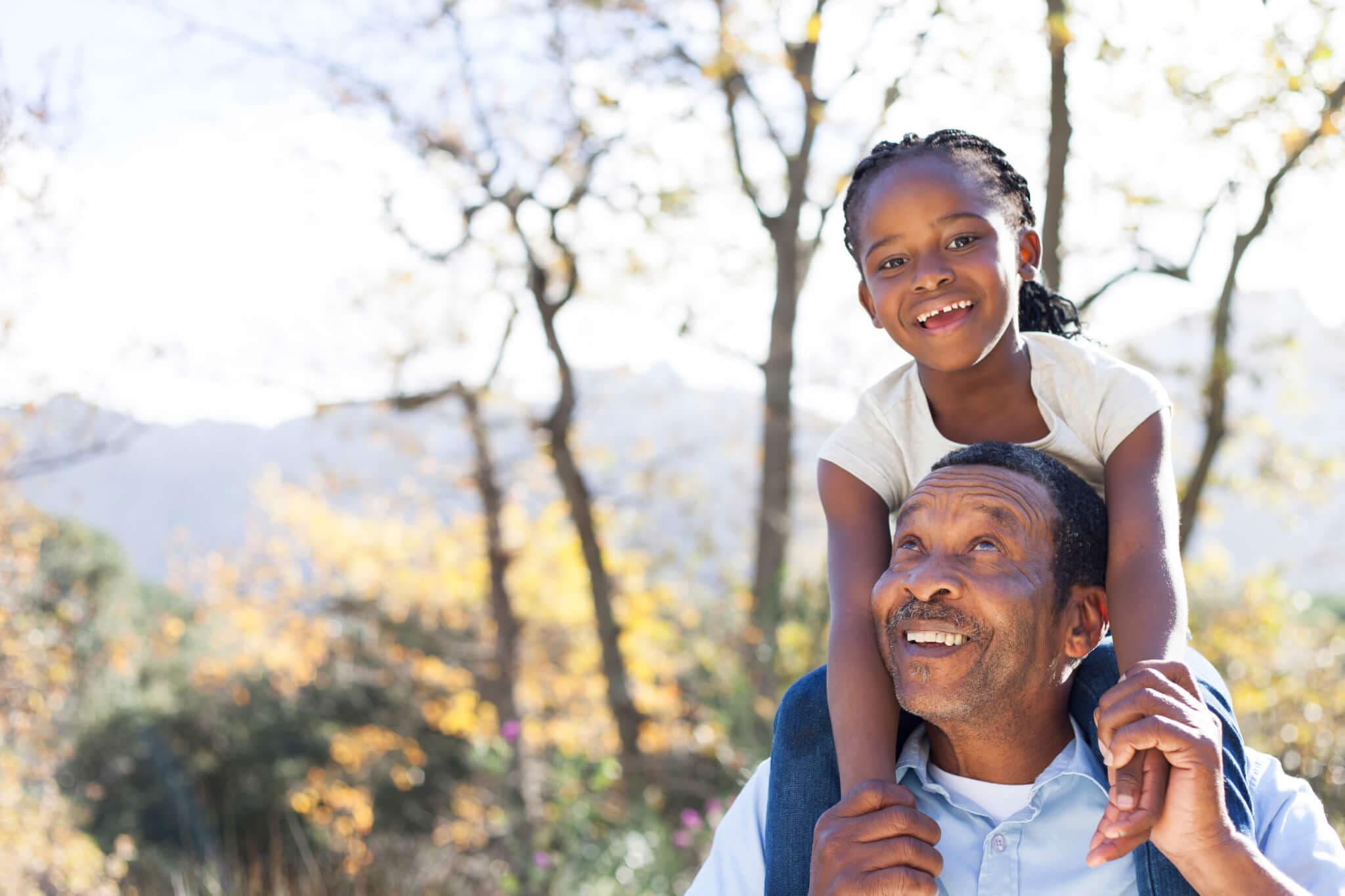 Man on a walk outside with child on his shoulders