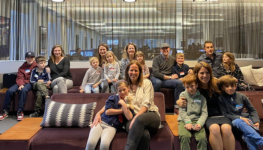 A group of kids with their parents sit on two rows of fuzzy couches in the Weber Shandwick New York office