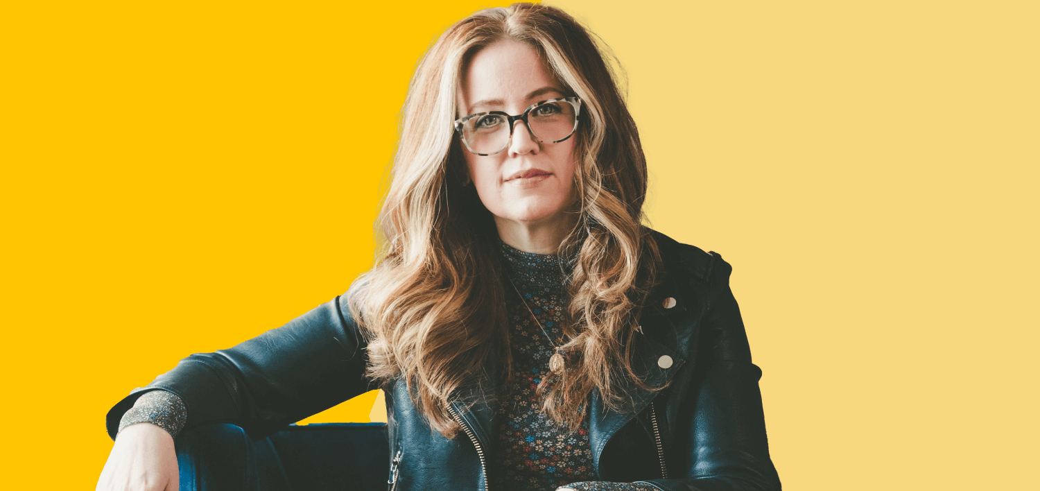 Image of a woman wearing a leather jacket and glasses, looking directly at the camera