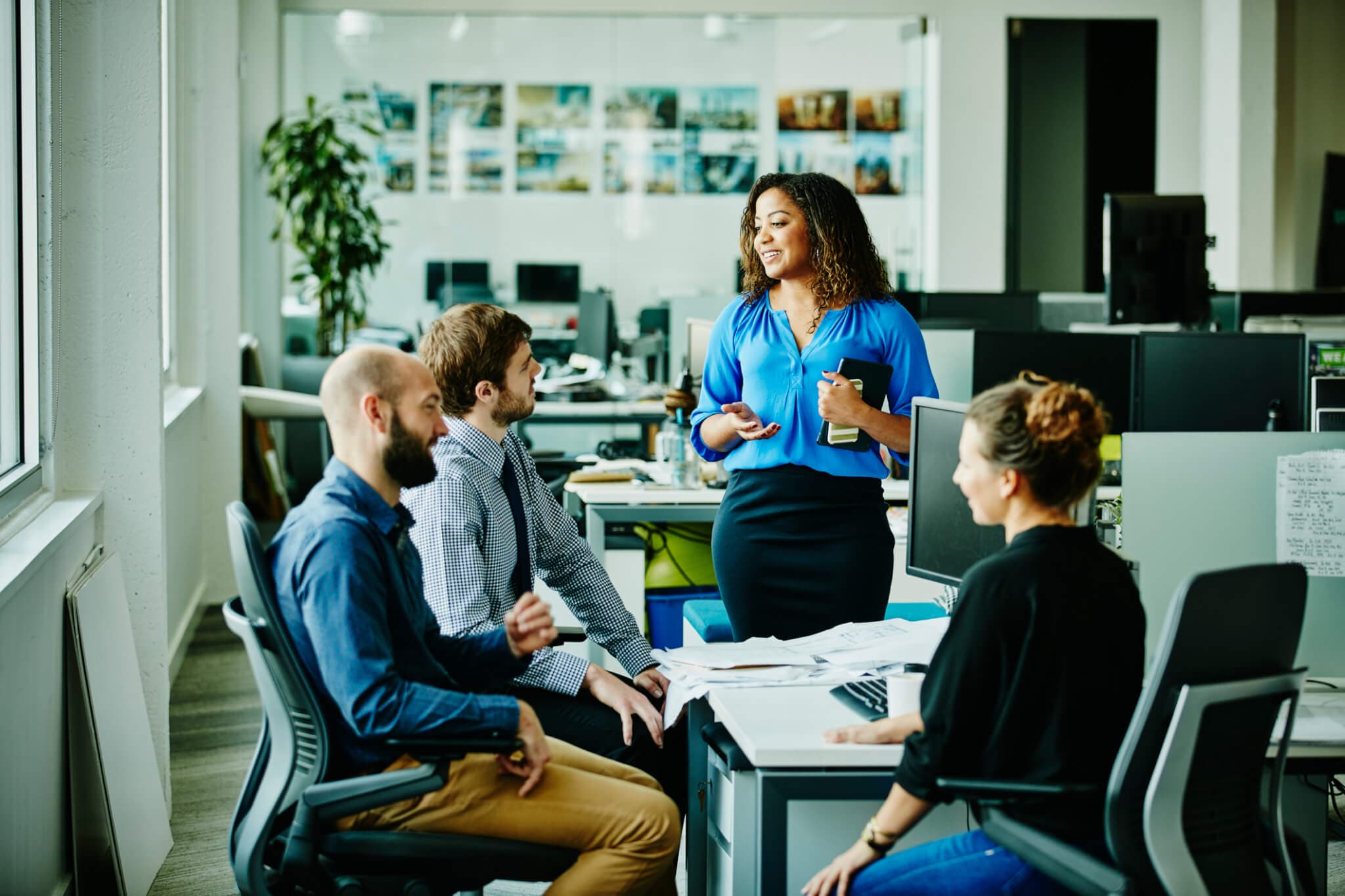 Businesswoman leading informal meeting with colleagues at office workstation