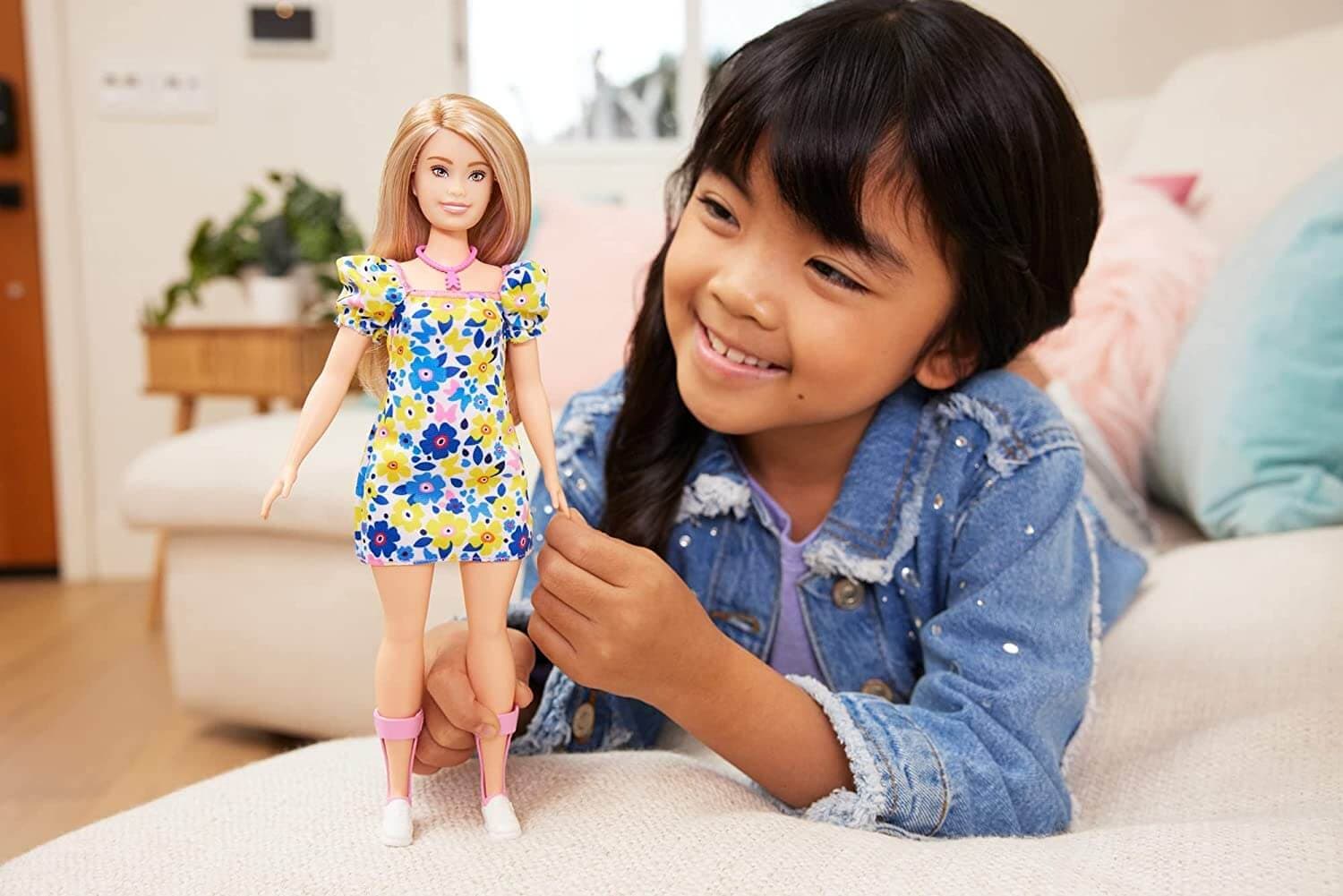 Image of an Asian girl in a jean jacket smiling as she plays with her new Barbie Down Syndrome Doll