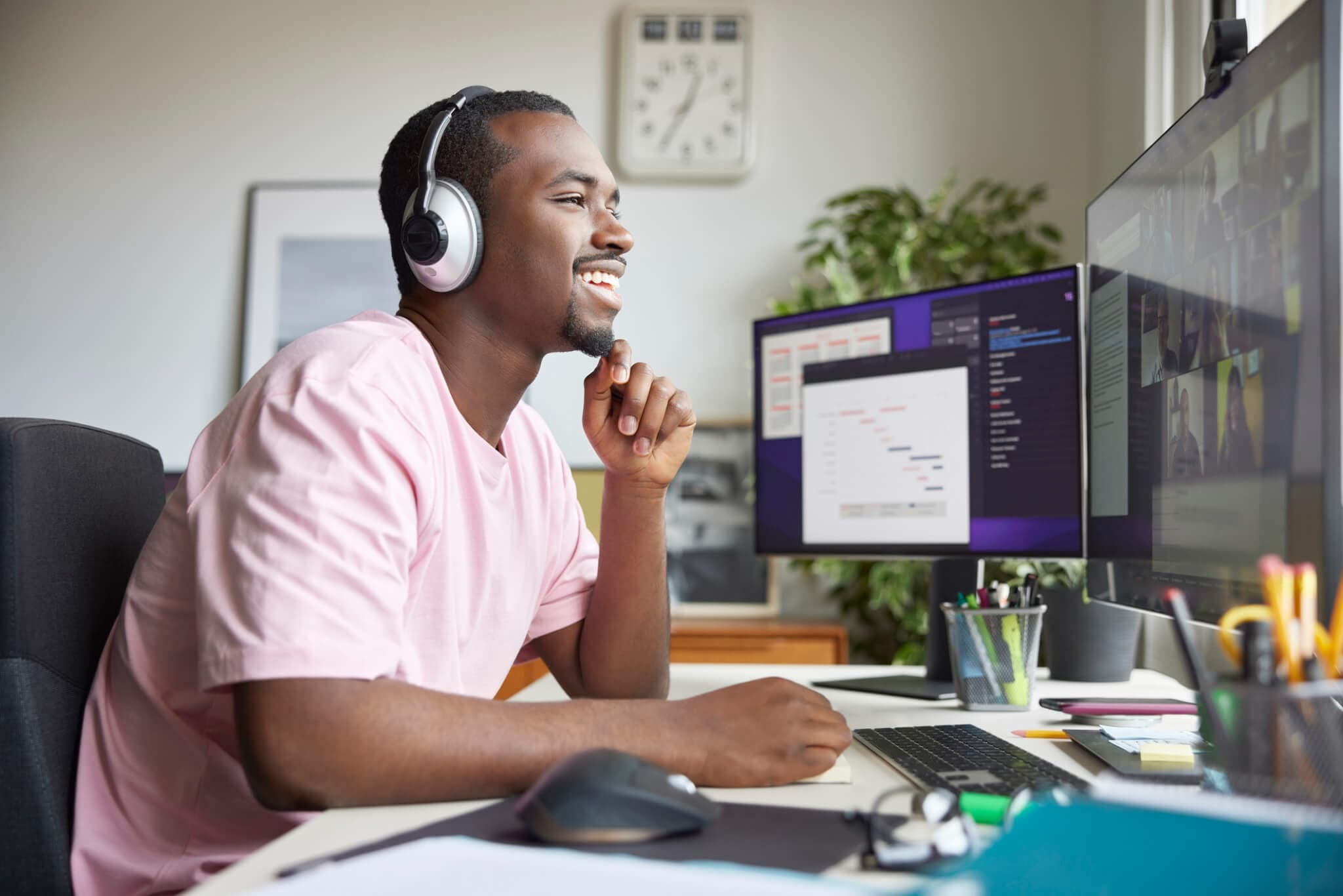 Smiling young entrepreneur sitting with diary looking at computer monitor. Businessman is on video call with colleagues at desk in apartment. He is telecommuting from home office.