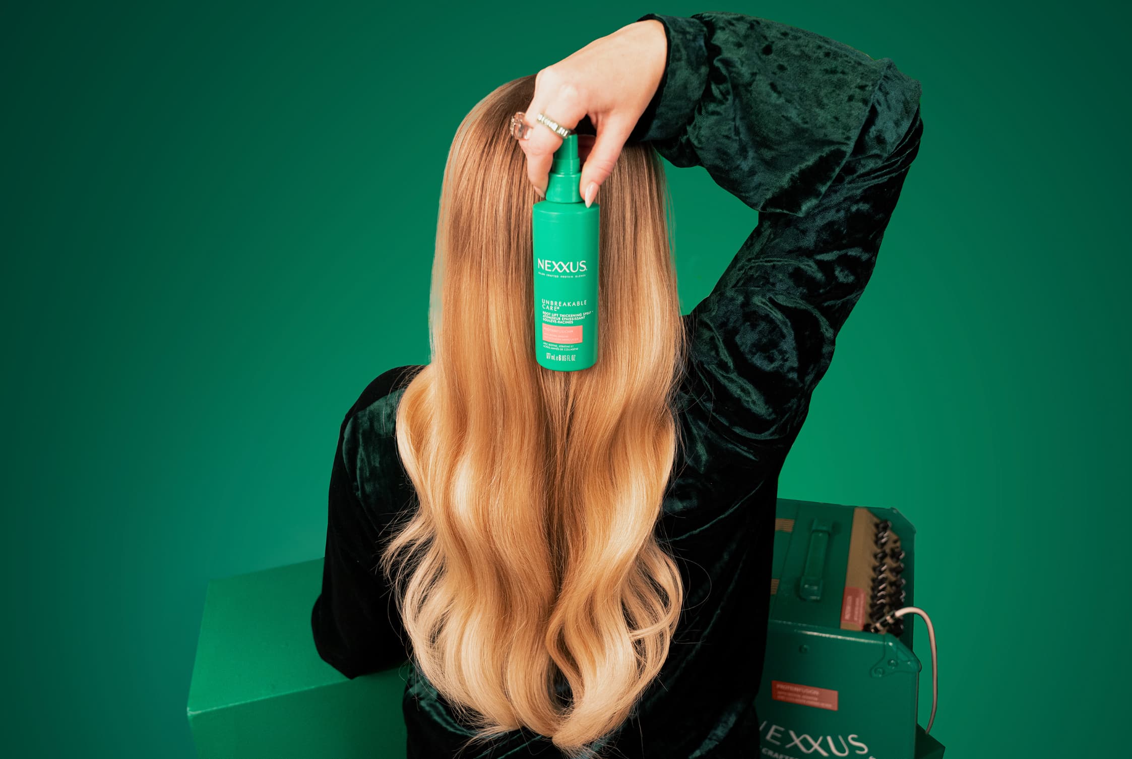Photo of Meghan Trainor holding up the Nexxus Unbreakable Care bottle on top of the back of her long wavy blonde hair