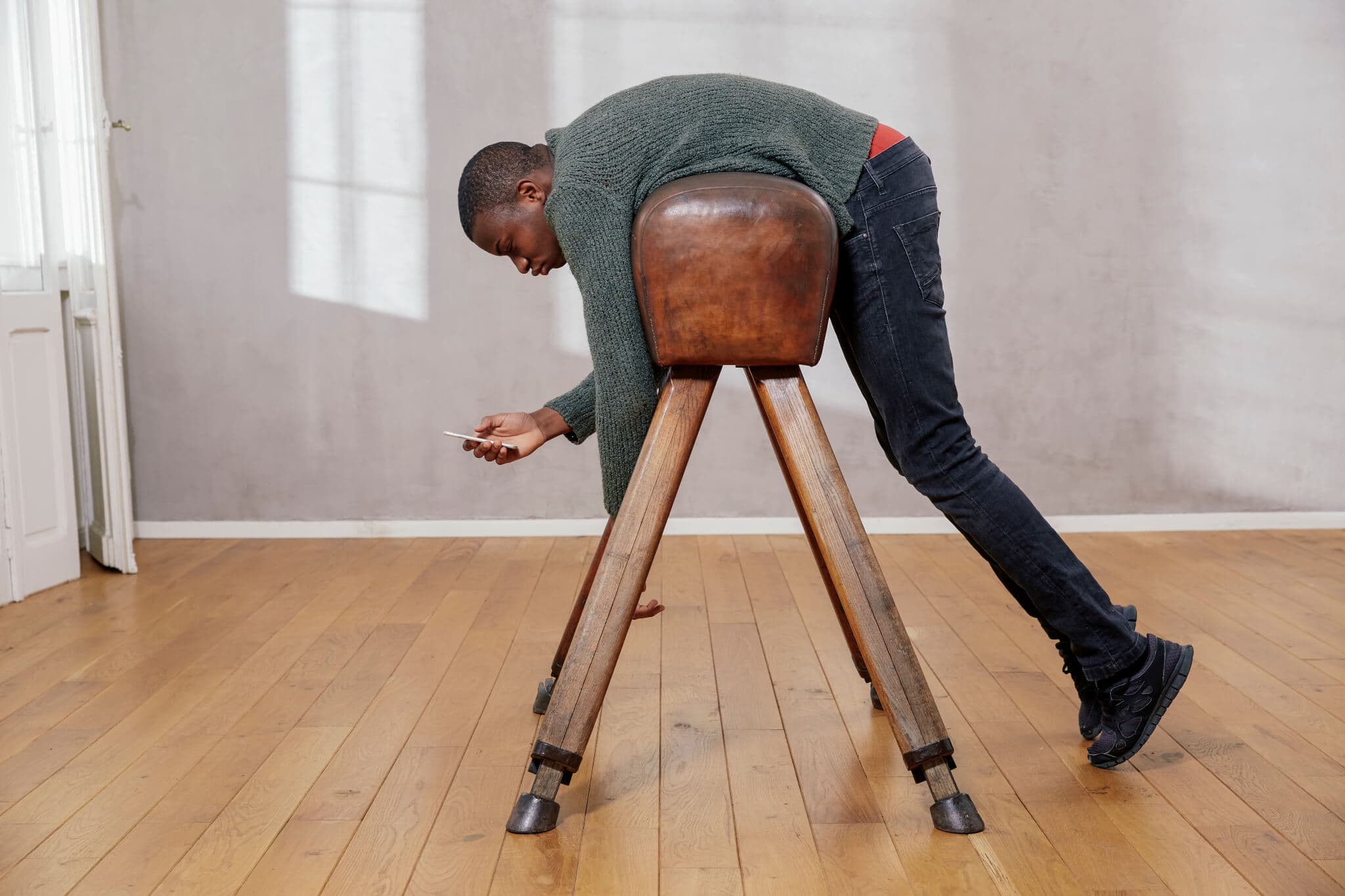 Young man hanging out on pommel horse looking at smartphone