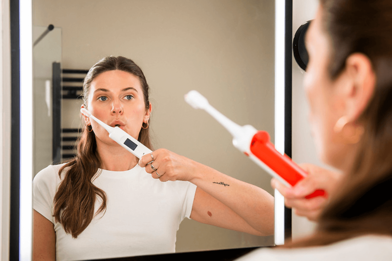 Image of a woman with long hair holding up the Brushalyser toothbrush in front of the bathroom mirror