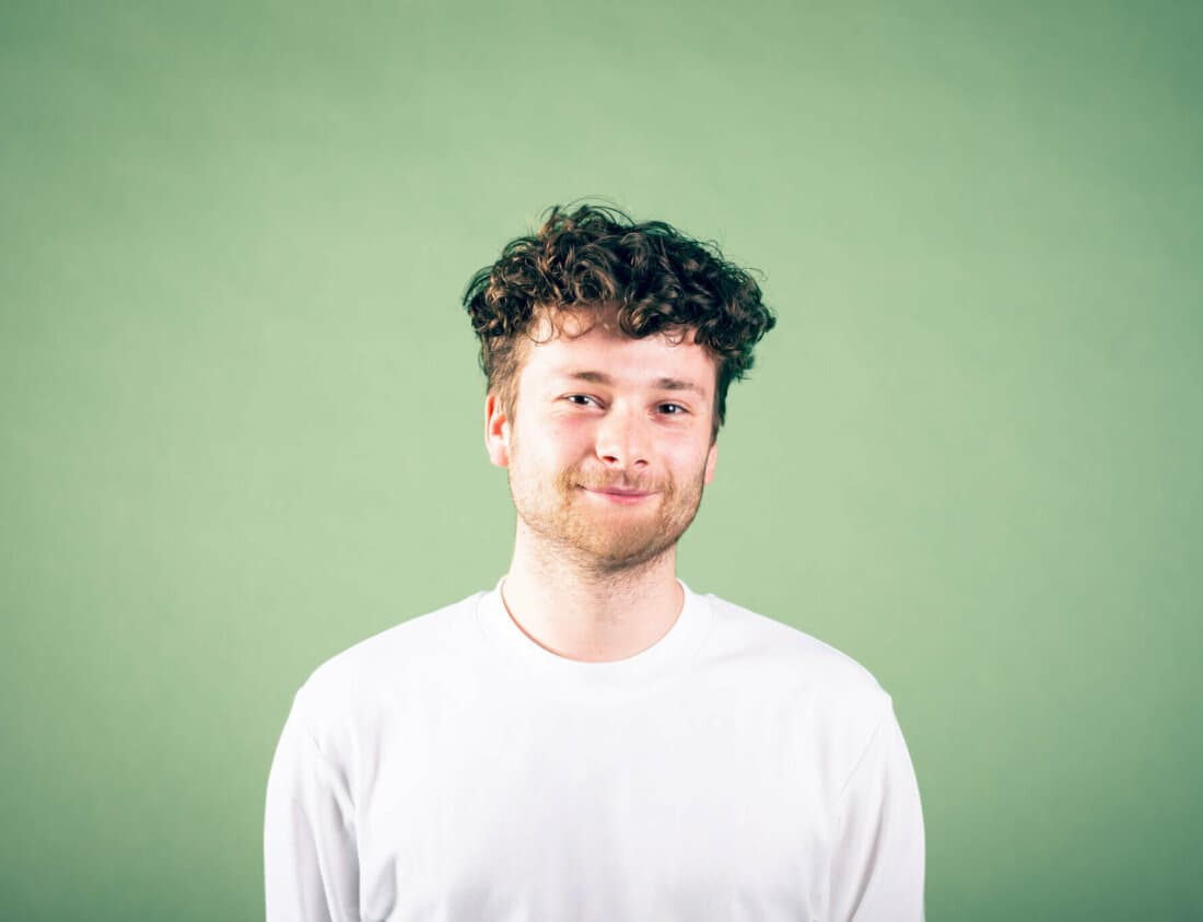 Image of a man with curly hair and a slight beard wearting a long sleeve shirt