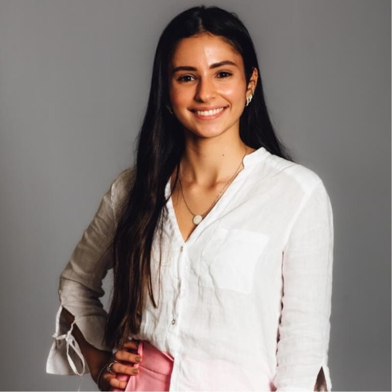 Image of a woman in a linen button up sirt with long dark straight hair, smiling directly at the camera with one hand on her hip