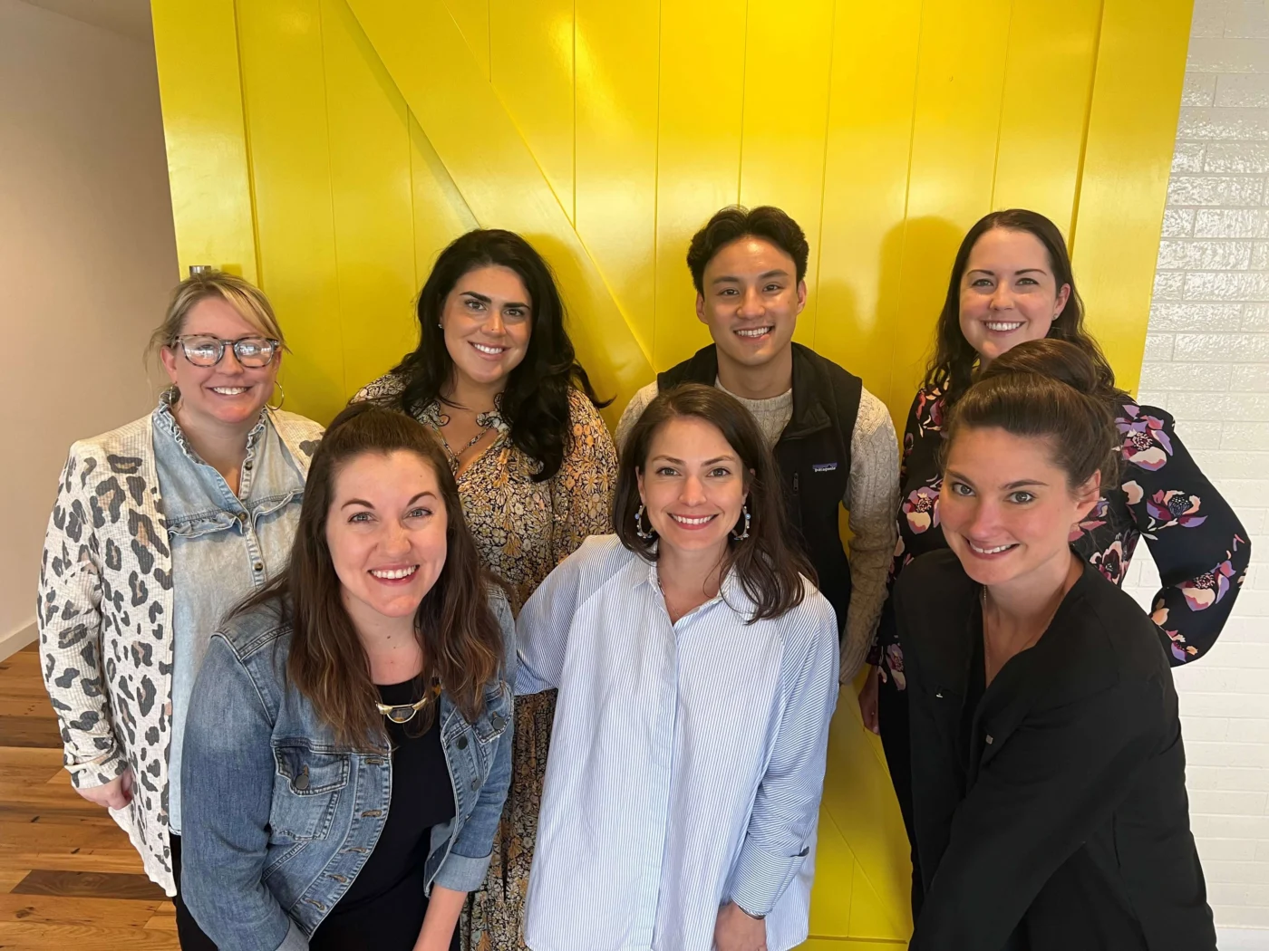 Weber Shandwick Dallas team gathered against yellow feature wall, highlighting team culture and collaborative office environment in Texas