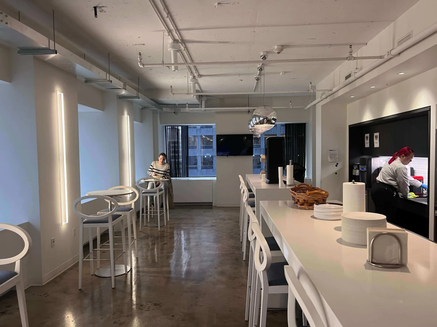 Weber Shandwick New York office kitchen and breakout area with bar seating, modern lighting and staff using shared workspace facilities