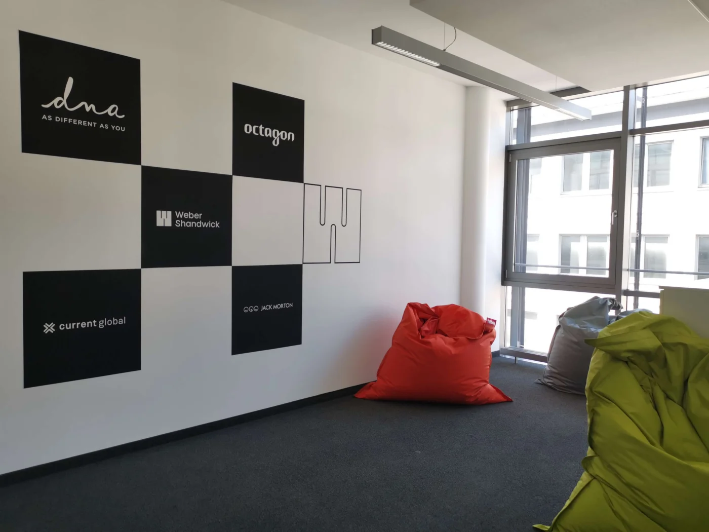 Weber Shandwick Munich office collaboration space with brand wall featuring partner logos and informal seating area