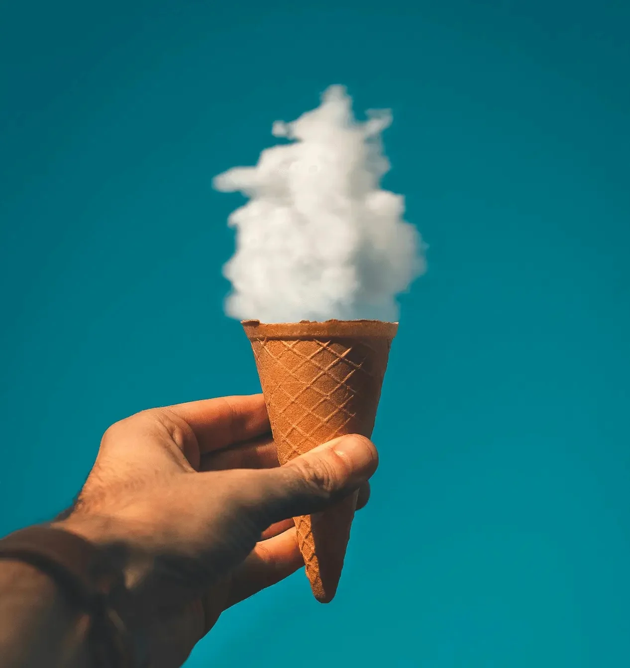 Hand holding empty ice cream cone topped with cloud against blue sky, symbolising creative ideas, imagination and culture-led brand storytelling