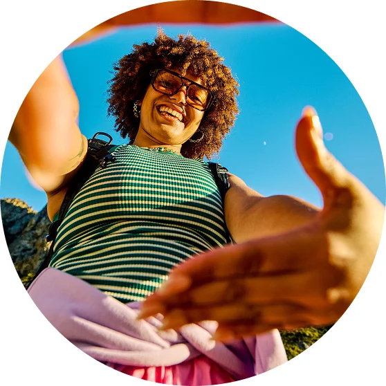 Smiling person reaching toward camera outdoors under blue sky, capturing human connection, cultural influence and authentic engagement in brand storytelling
